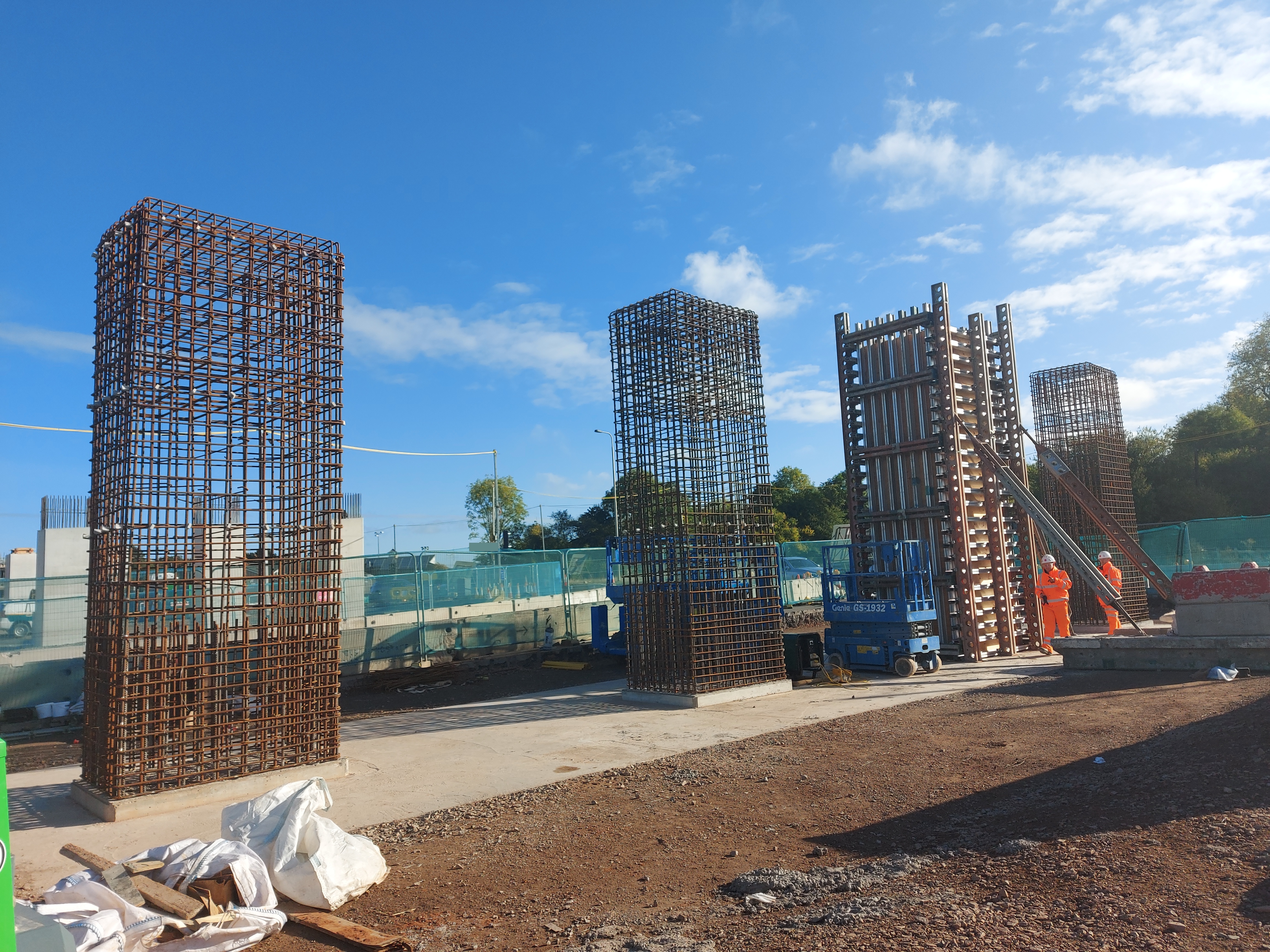 Three free-standing column reinforcement cages with crew working a fourth, on a sunny site