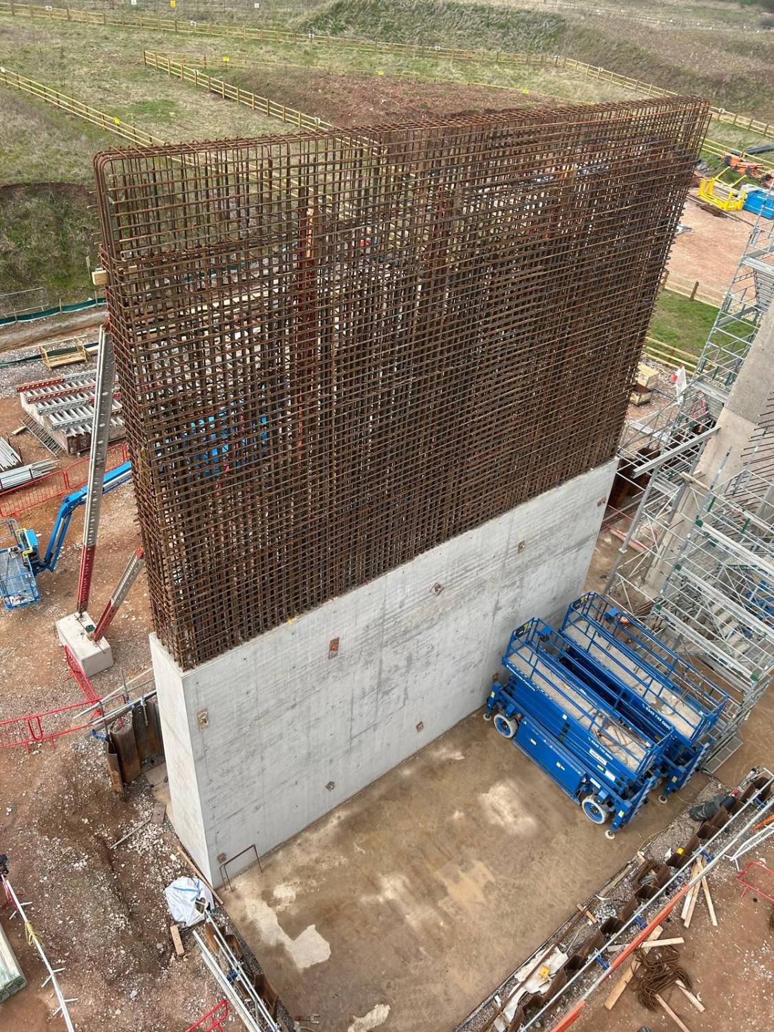 Tall wall reinforcement cage rising above a freshly poured concrete wall, viewed from elevation