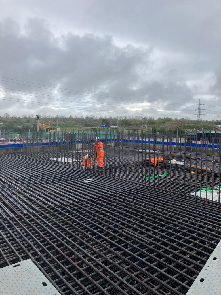 Wide bridge deck reinforcement mat with two Quick-Steel-Fix fixers in the distance under a dramatic grey sky