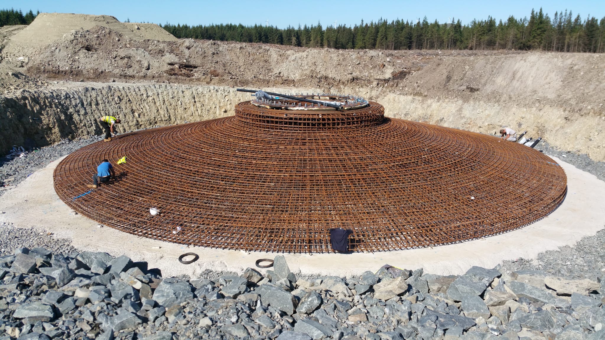 Wind turbine foundation reinforcement mat viewed from elevation, surrounded by quarry landscape